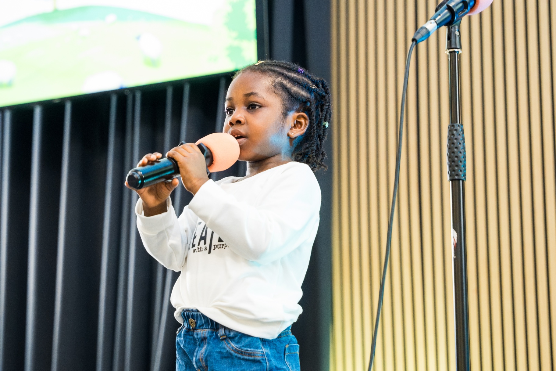Little girl holding a microphone and singing during Kids and Youth presentation